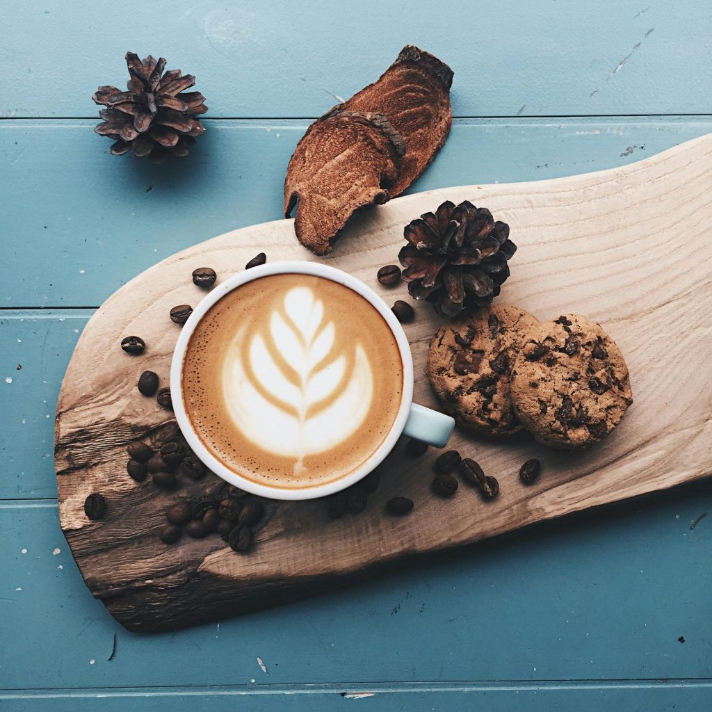 A cappuccino with latte art served with cookies on a rustic wooden board, perfect for coffee lovers.